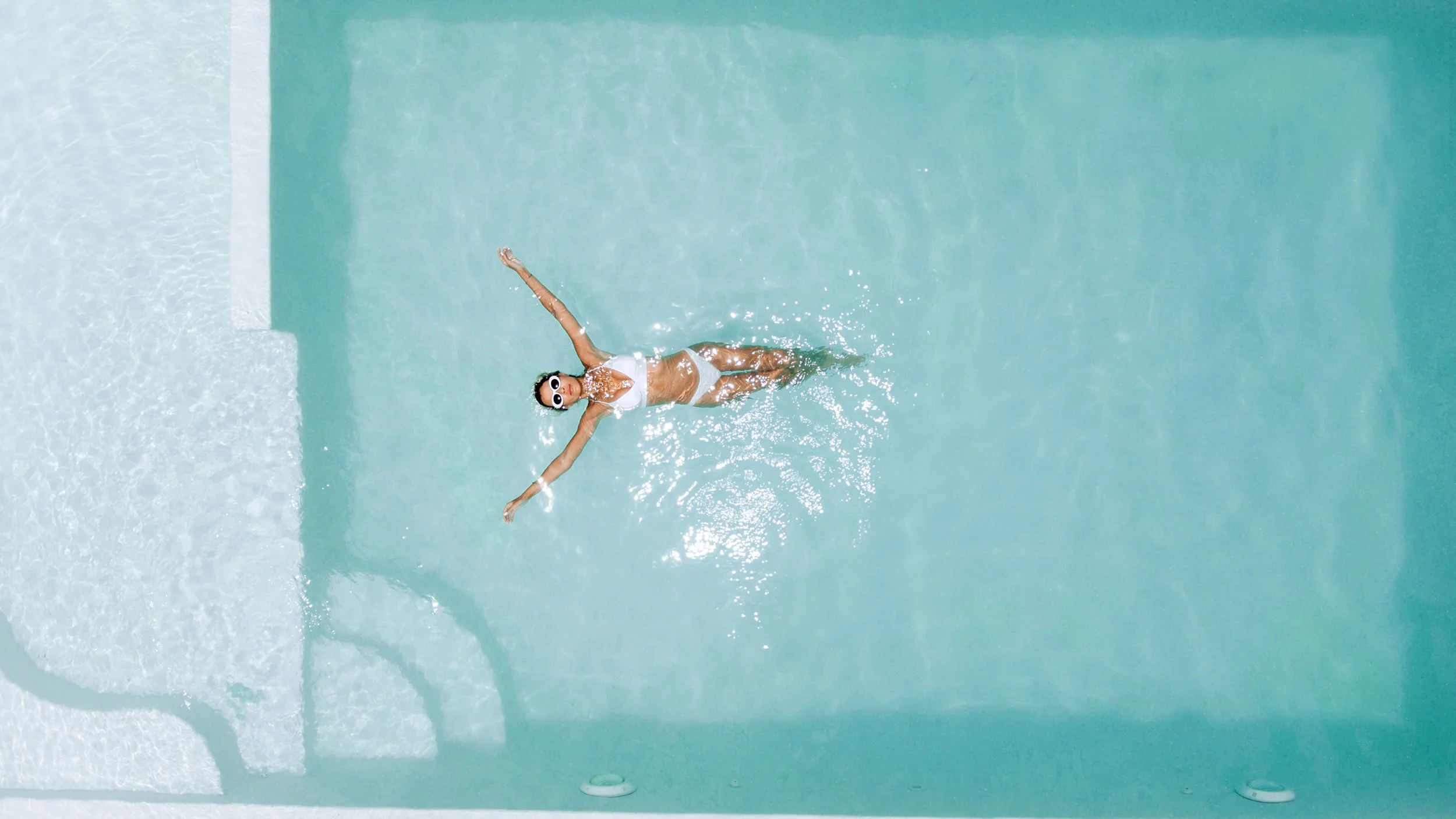 Overhead view of a woman relaxing in a luxury resort pool representing hospitality, lifestyle, and elevated brand experiences.