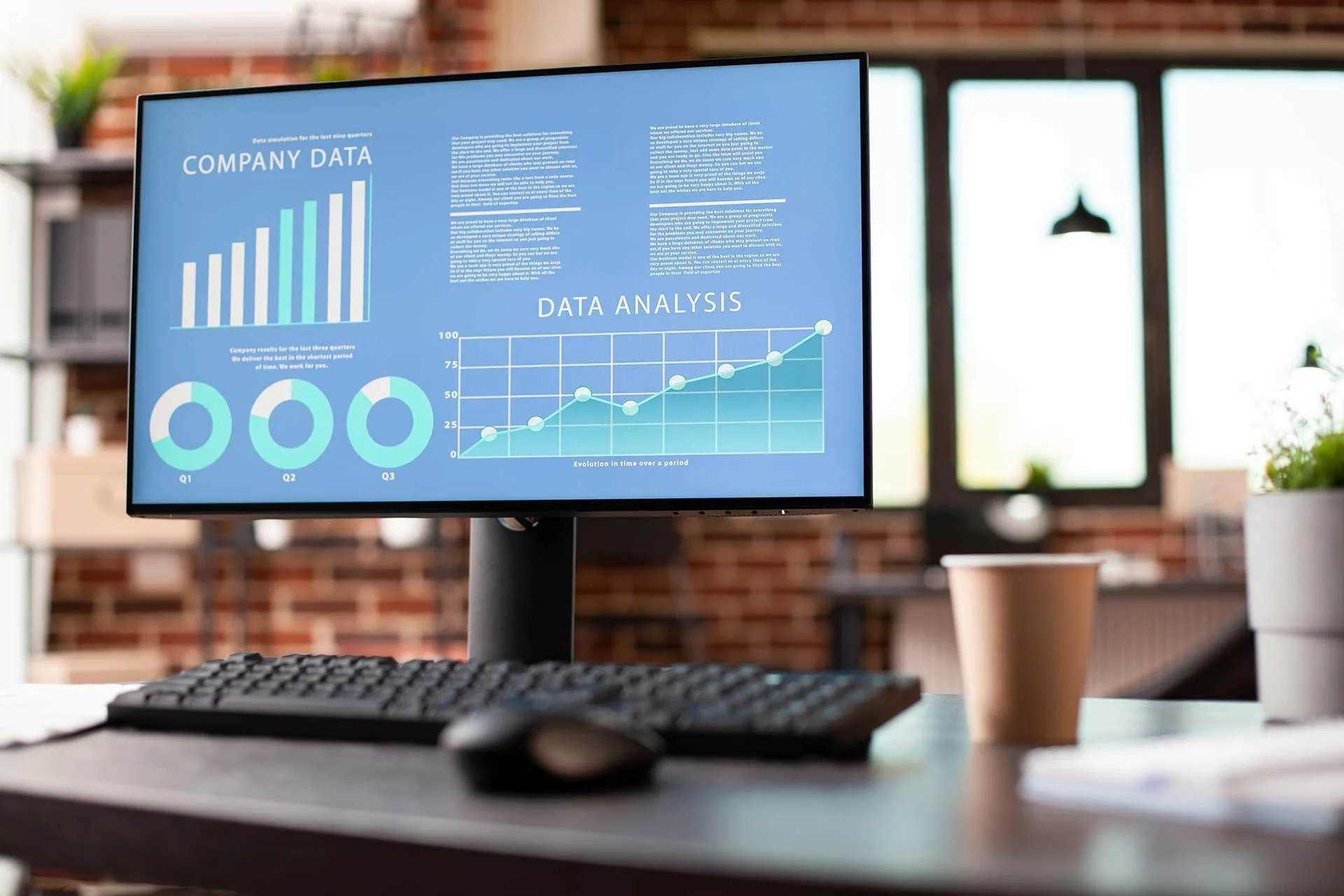 Computer monitor displaying data analysis charts in a modern office with large windows and brick wall background.