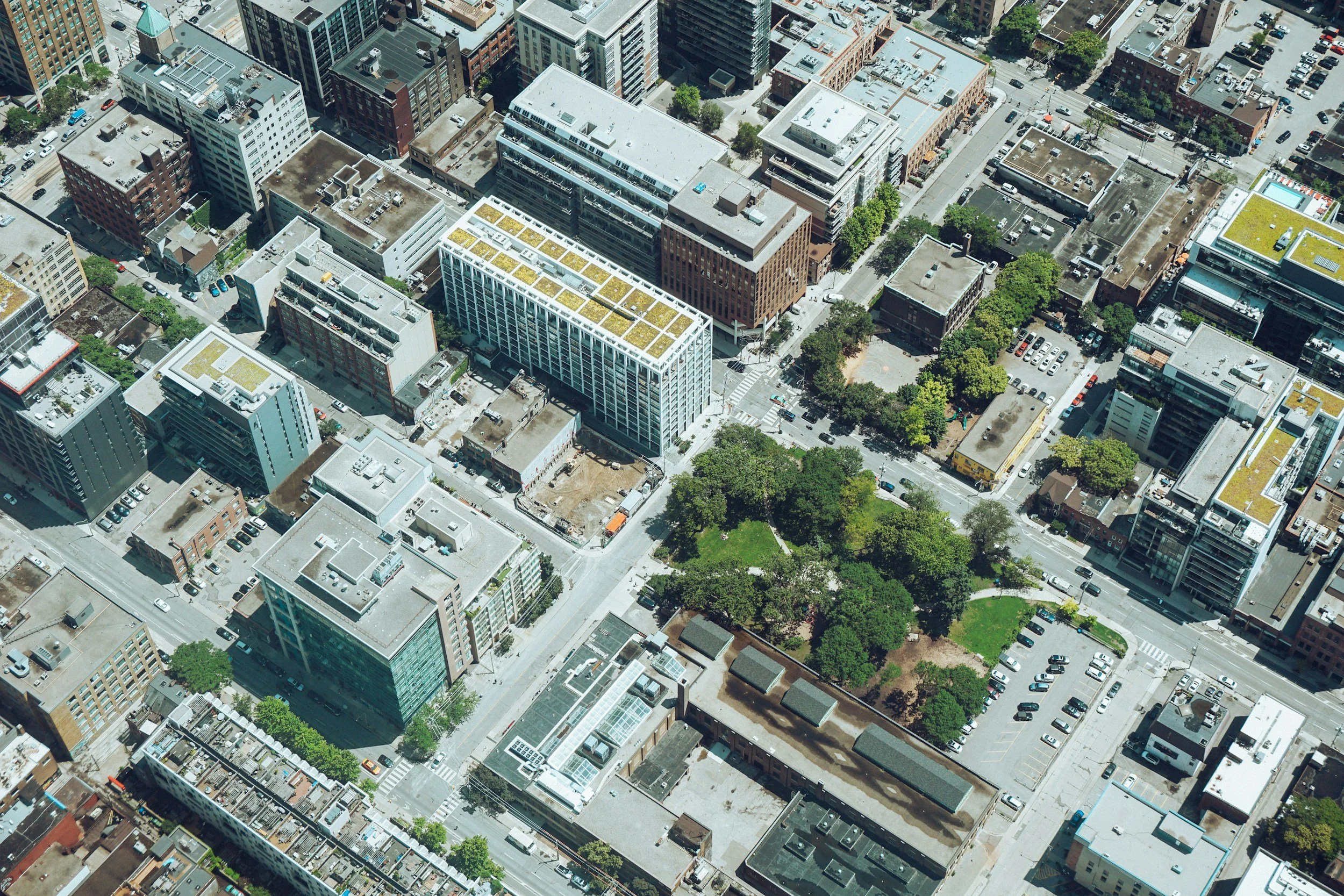 Aerial view of a city block showing high-rise buildings, parking lots, and a green park area with trees.