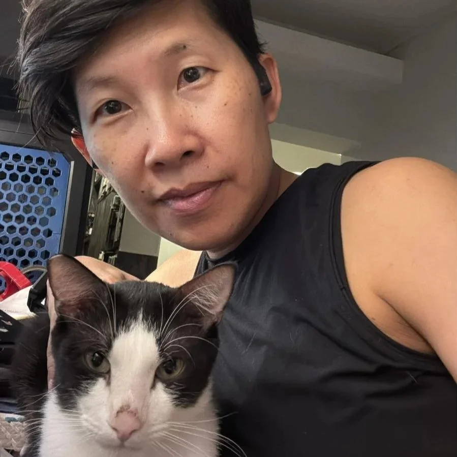 A person with short dark hair taking a selfie with a black and white cat in an indoor setting.