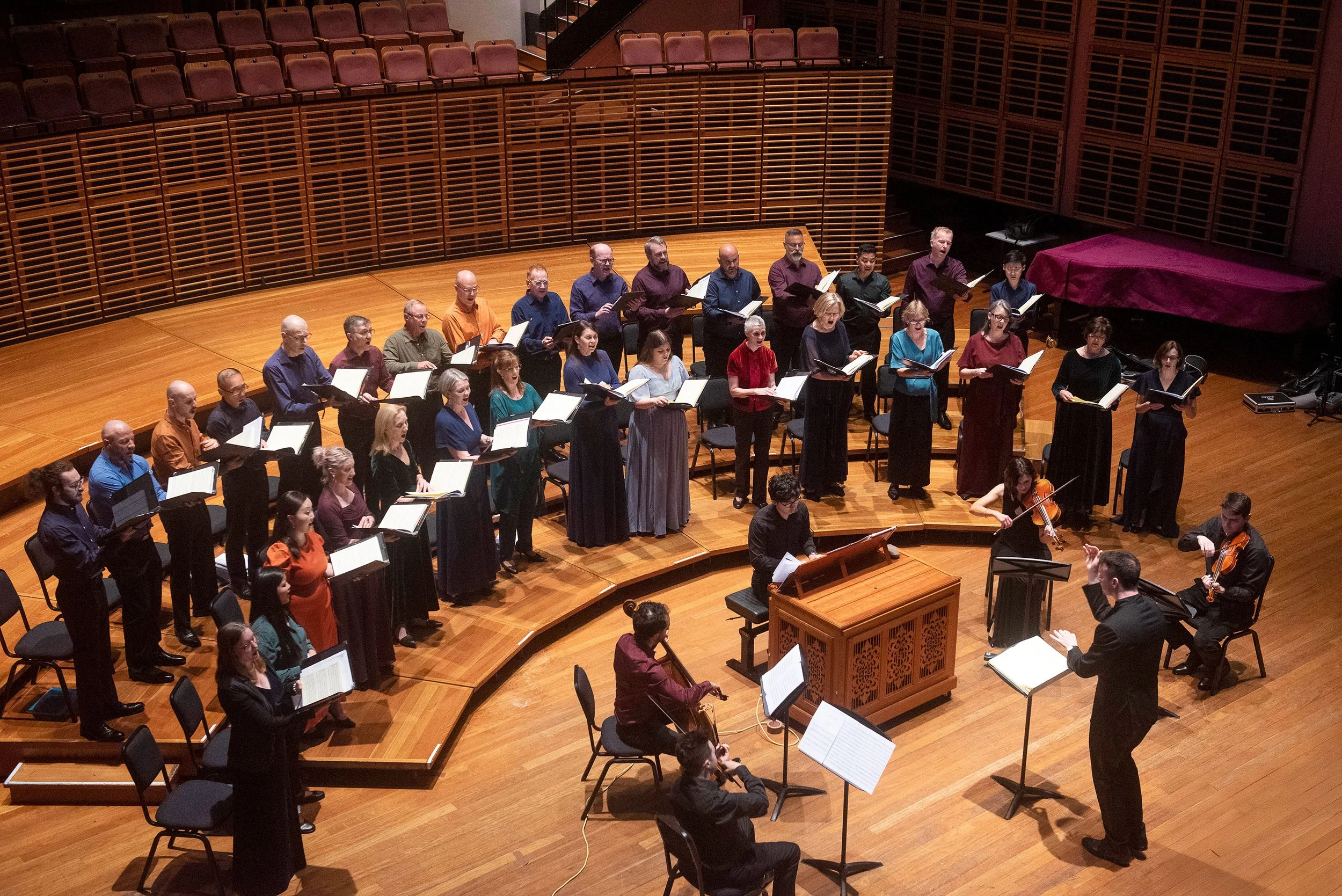 Sydney Chamber Choir, conducted by Sam Allchurch, performing on stage at Sydney Conservatorium of Music, a concert hall with wooden floors and seating.