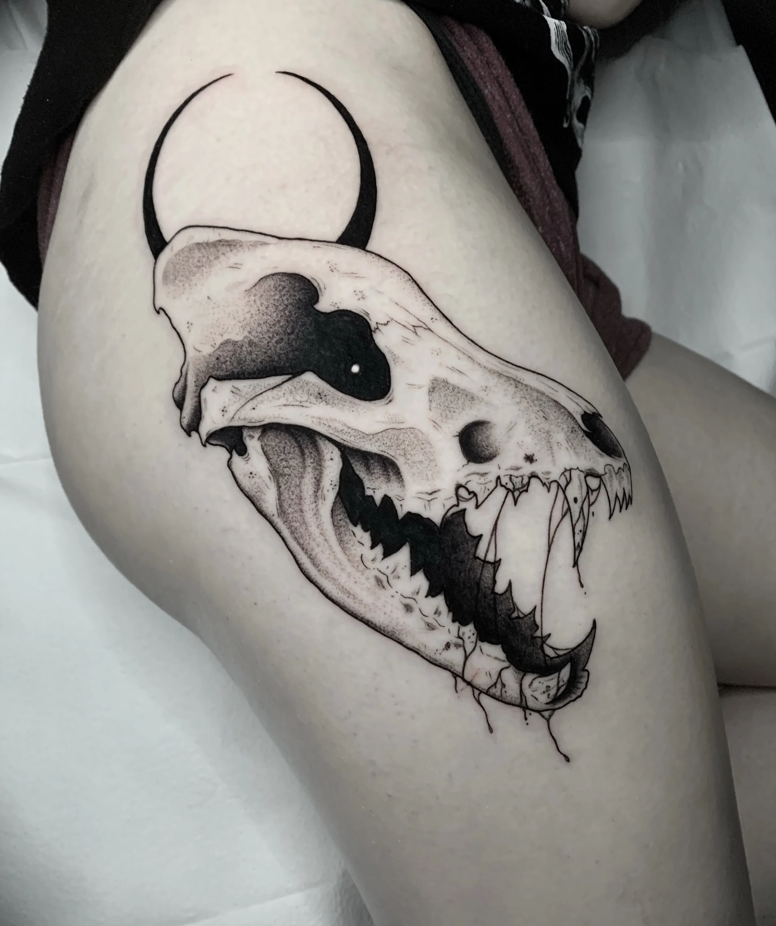 Black and gray tattoo of a skull with sharp teeth and exaggerated features on a person's thigh.