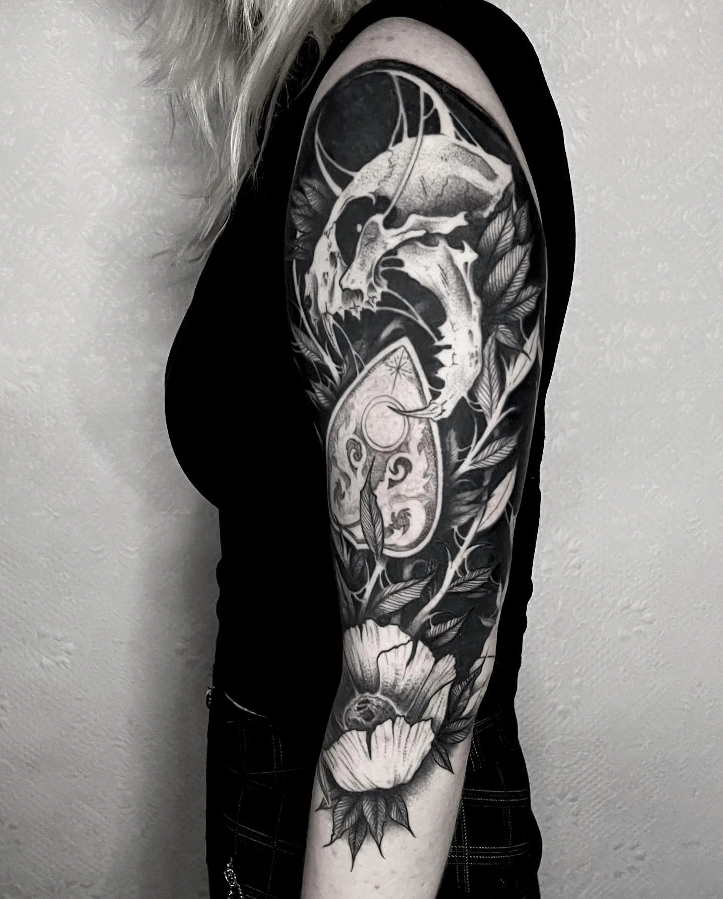 Black and white tattoo sleeve featuring a dragon, leaves, and floral elements on a person's arm.
