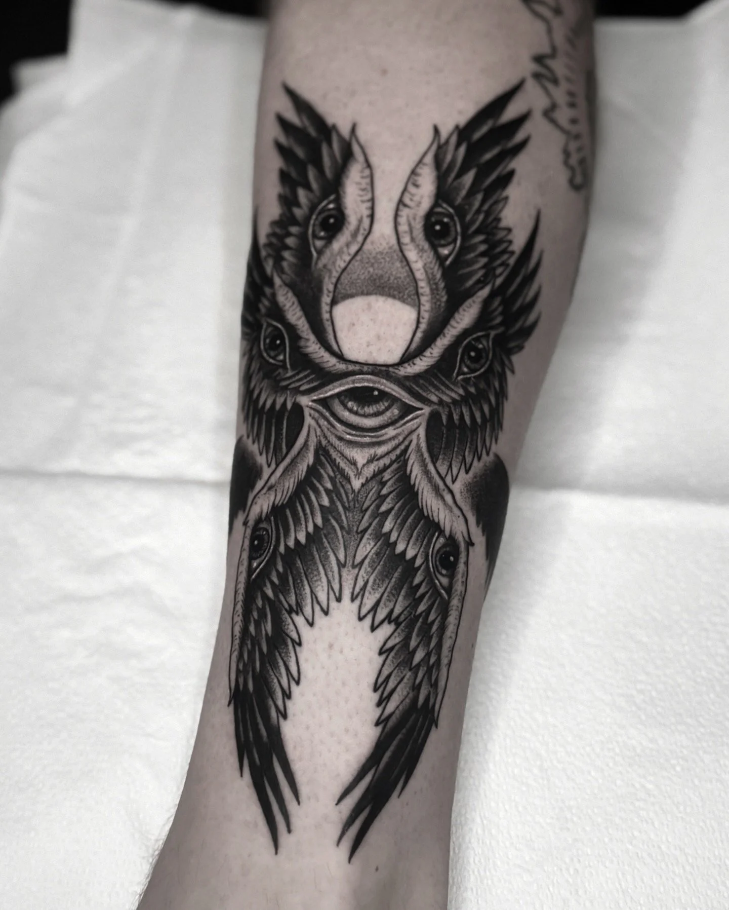 Tattoo of a wolf's head with multiple eyes and feathers, in black and gray ink.
