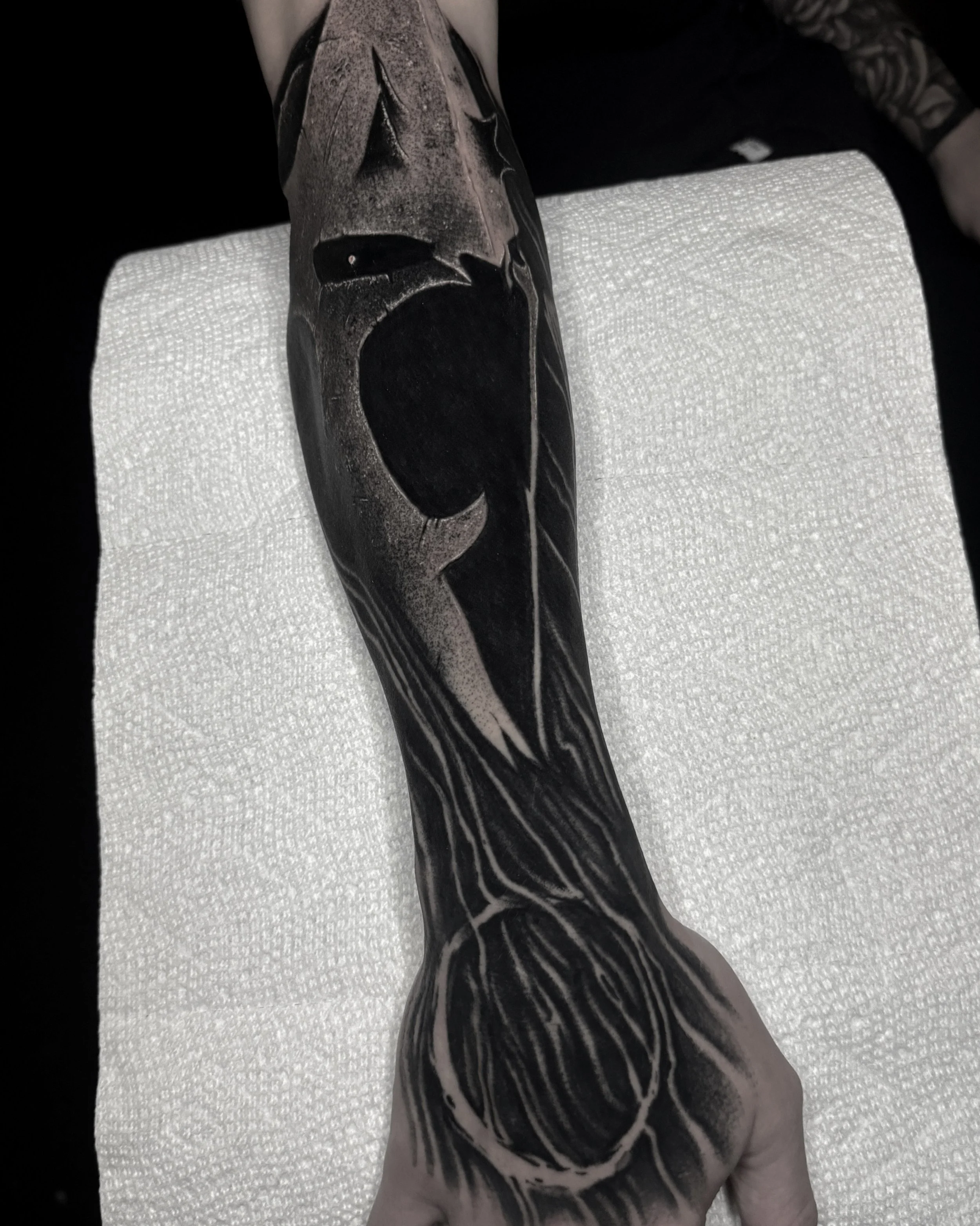 A person's arm with a black and gray tattoo of a skull and intricate line designs.