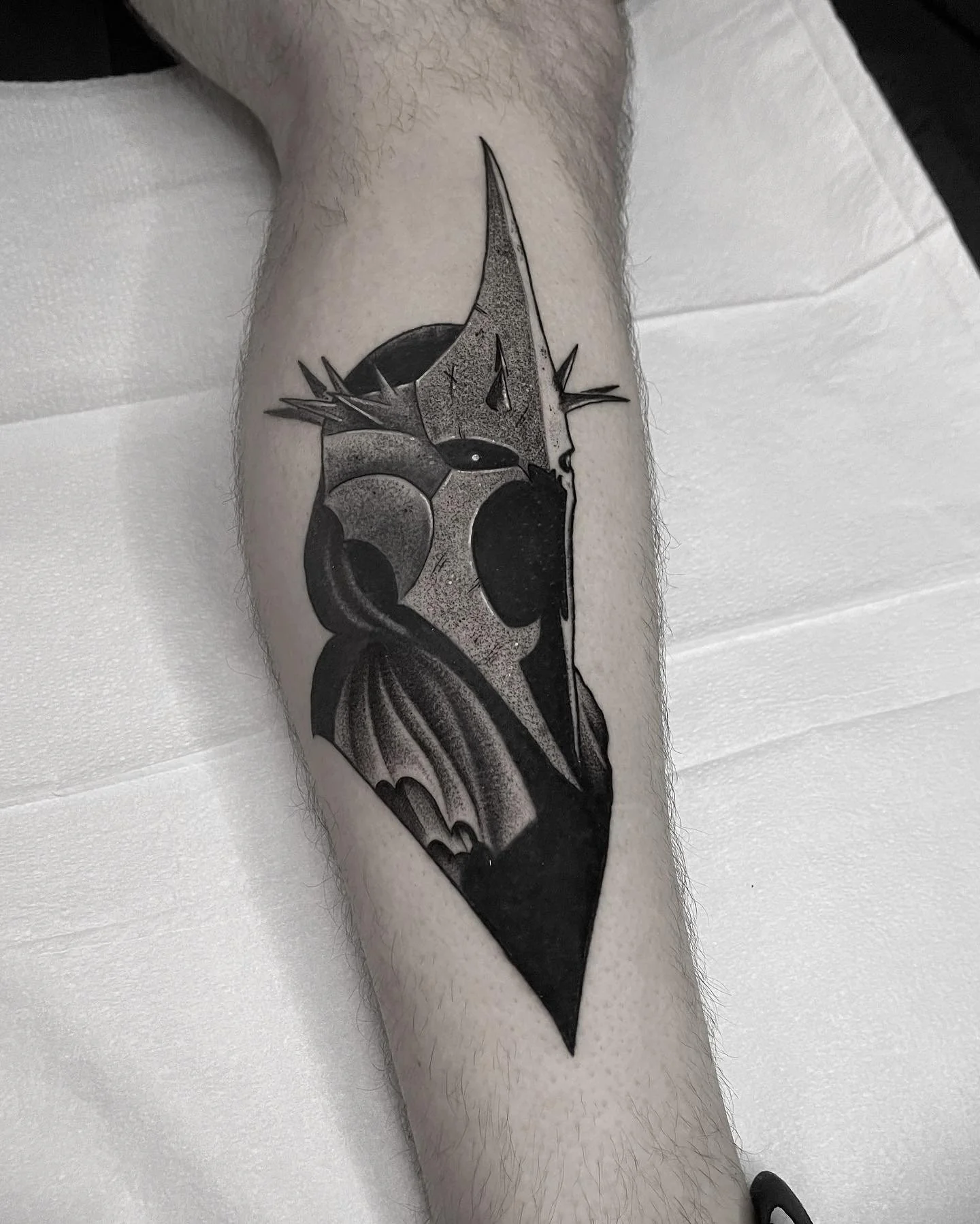 Black and gray tattoo of a skull with bat wings and a long, pointed crown-like feature on top, on a person's forearm.
