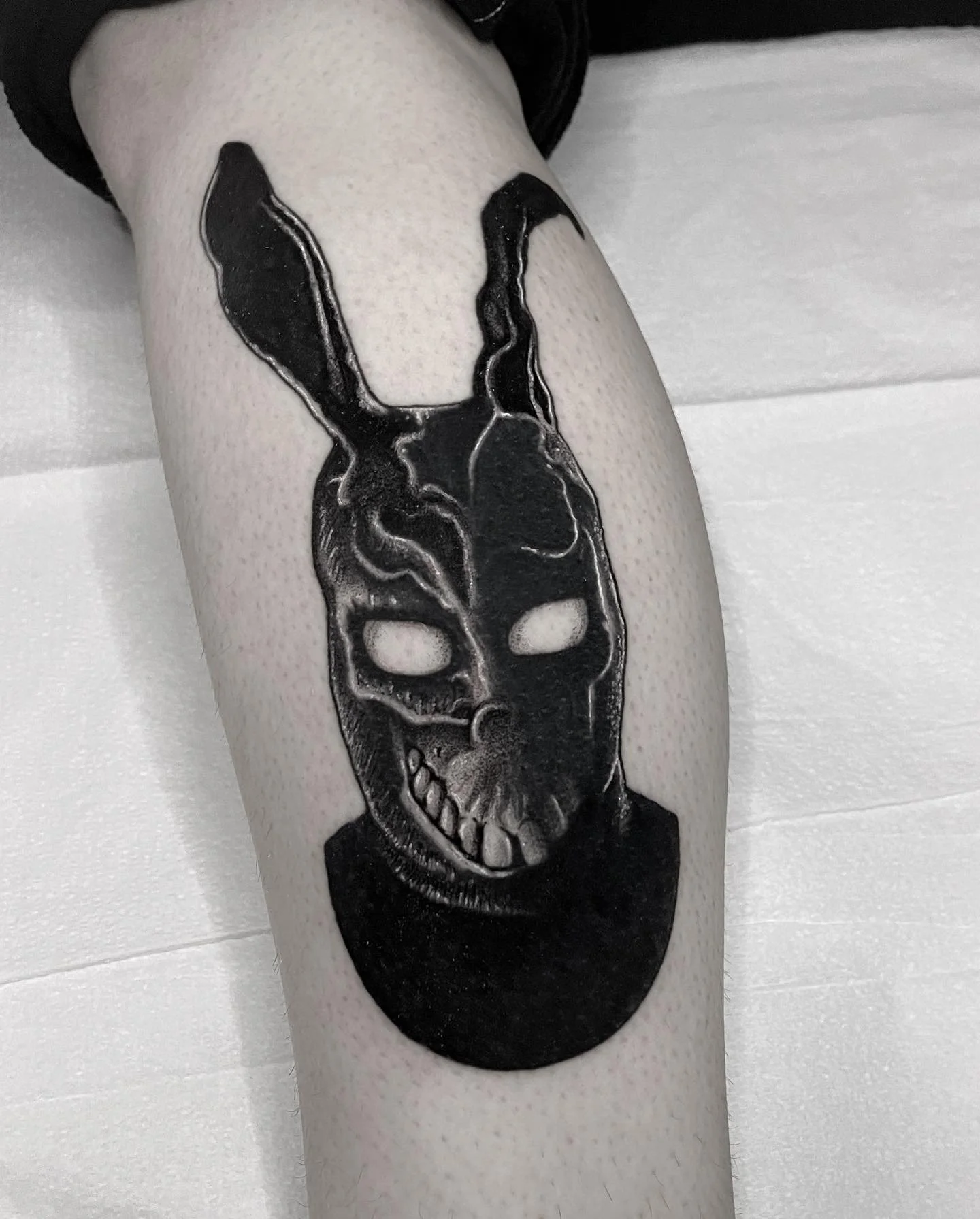Tattoo of a black skull with rabbit ears and hollow eyes on a person's leg.
