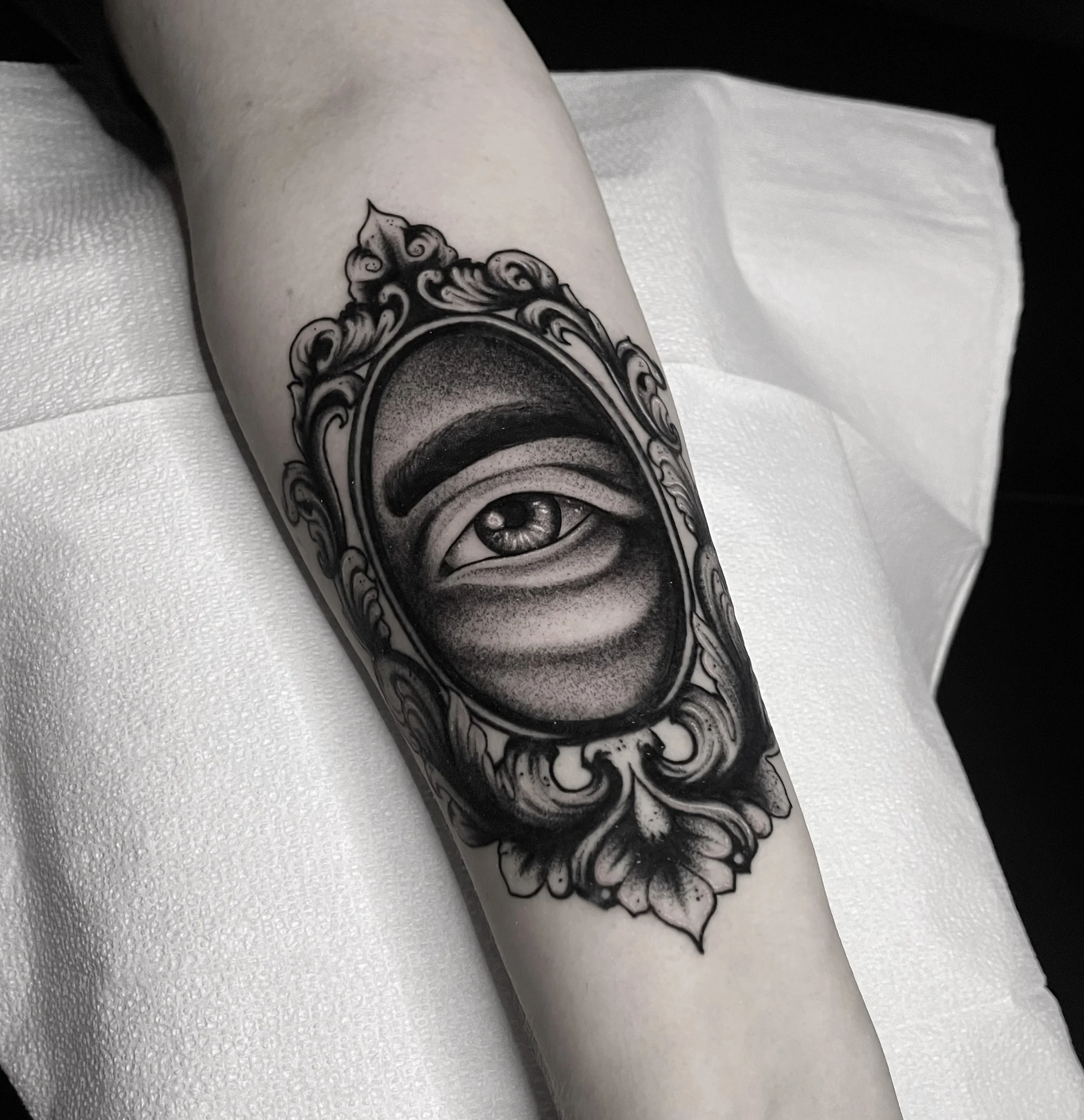 Tattoo of an eye within an ornate, decorative frame on a person's forearm.