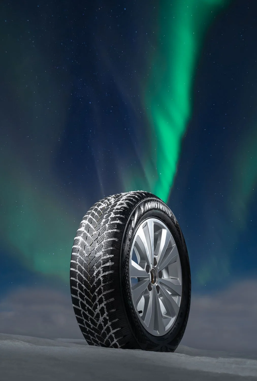 A car tire standing upright on snow with the northern lights and starry night sky in the background.