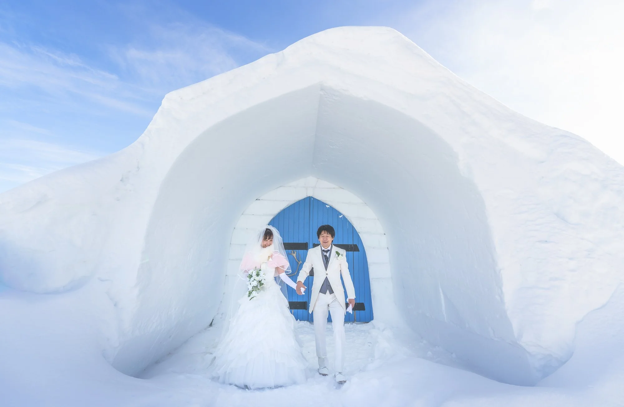 Bride and groom in wedding at Saariselkä, attire walking hand-in-hand through an ice tunnel with a blue door