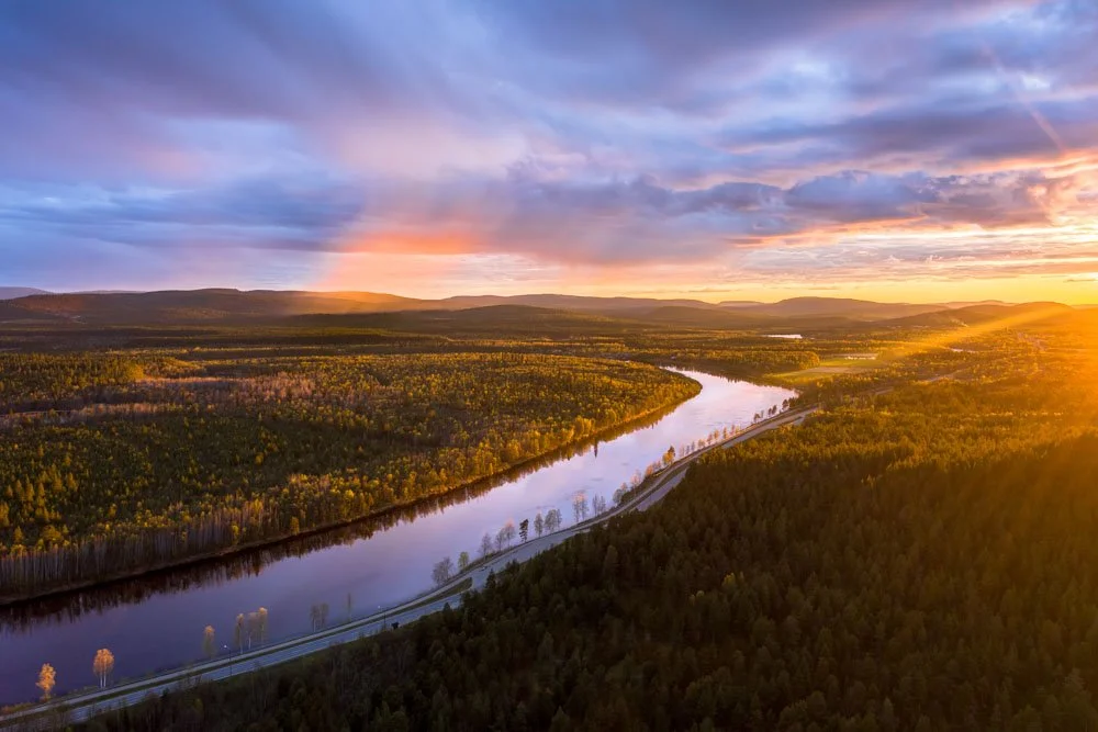 A scenic river winding through a vast forested landscape during sunset with colorful clouds in the sky.