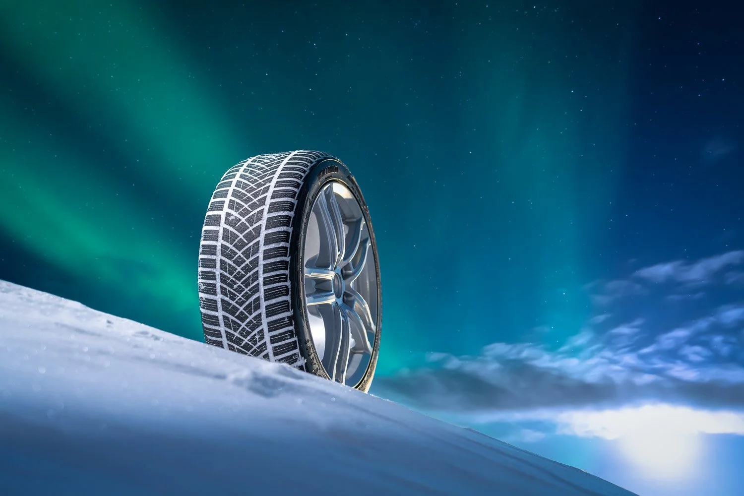 Close-up of a car tire on snow with the Northern Lights and starry night sky in the background.