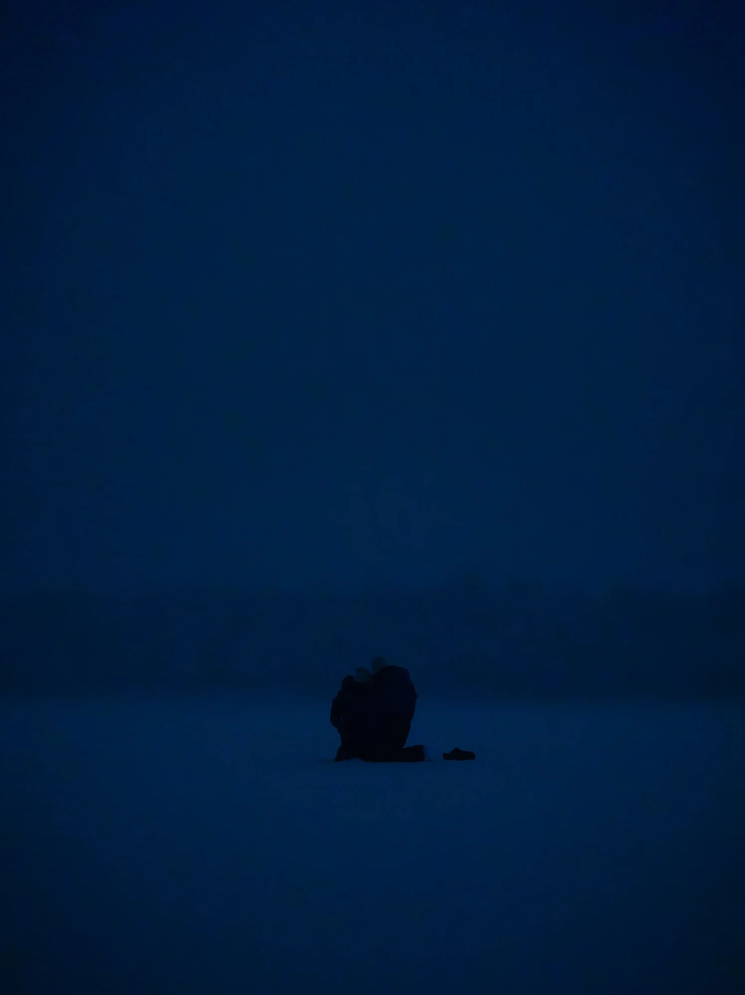 A person sitting on a rock in a vast, dark, and empty landscape during nighttime.