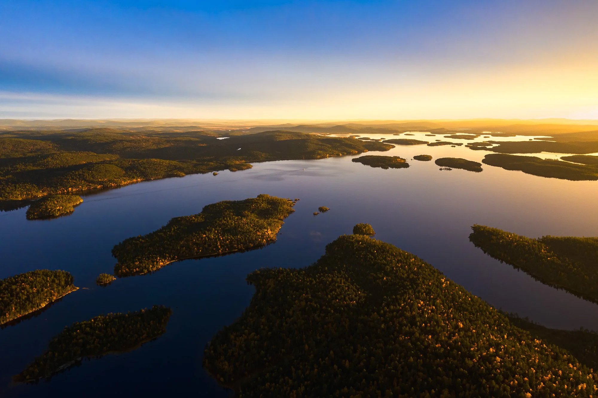 Aerial view of numerous small islands and a large lake during sunset with blue sky and clouds.