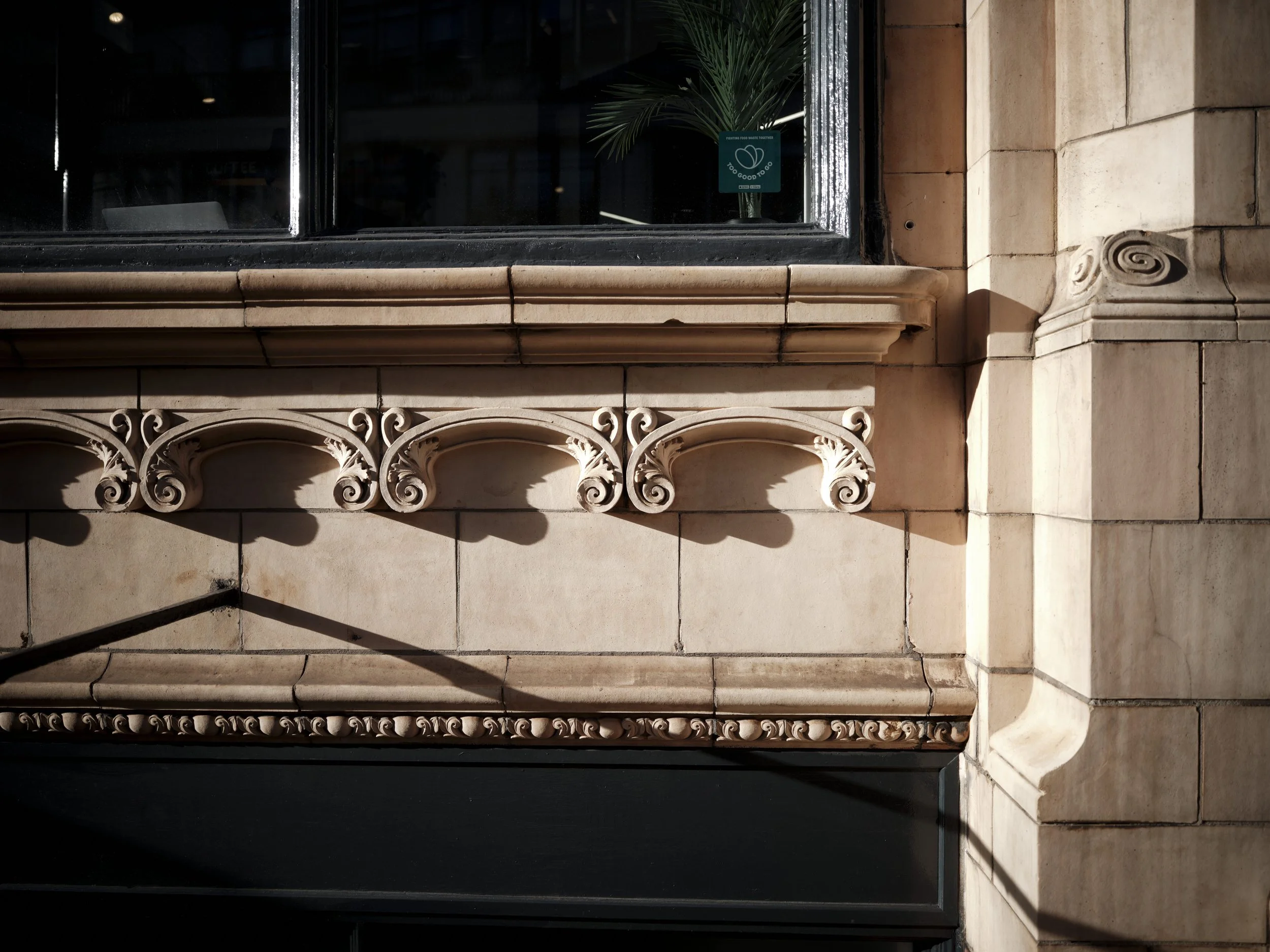 Close-up of old stone building facade with decorative architectural elements, black window, and a sign in the window.