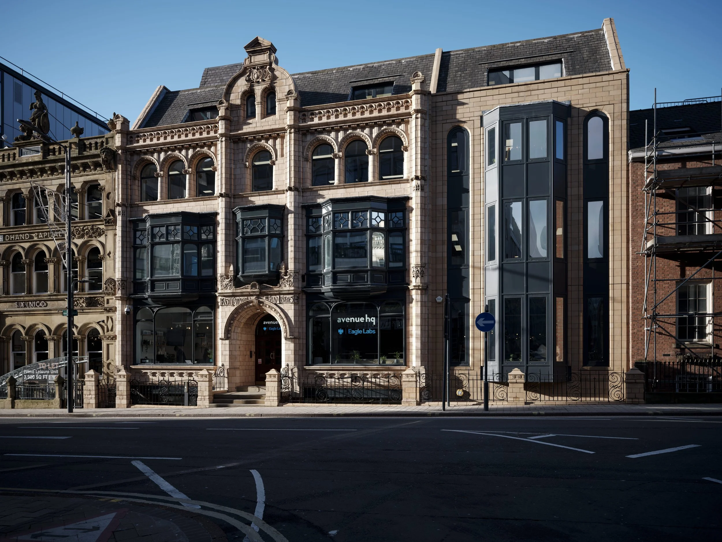 Historic building with ornate stone facade, large bay windows, and a modern glass elevator extension, situated on a city street.