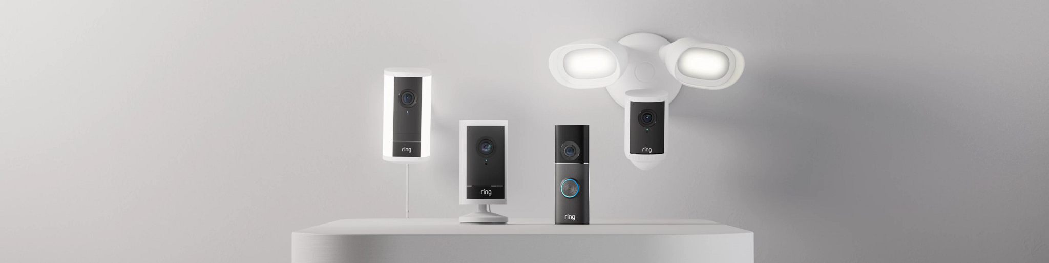 Display of four Ring security cameras in black and white, mounted on a white wall with a cloud-shaped light fixture.