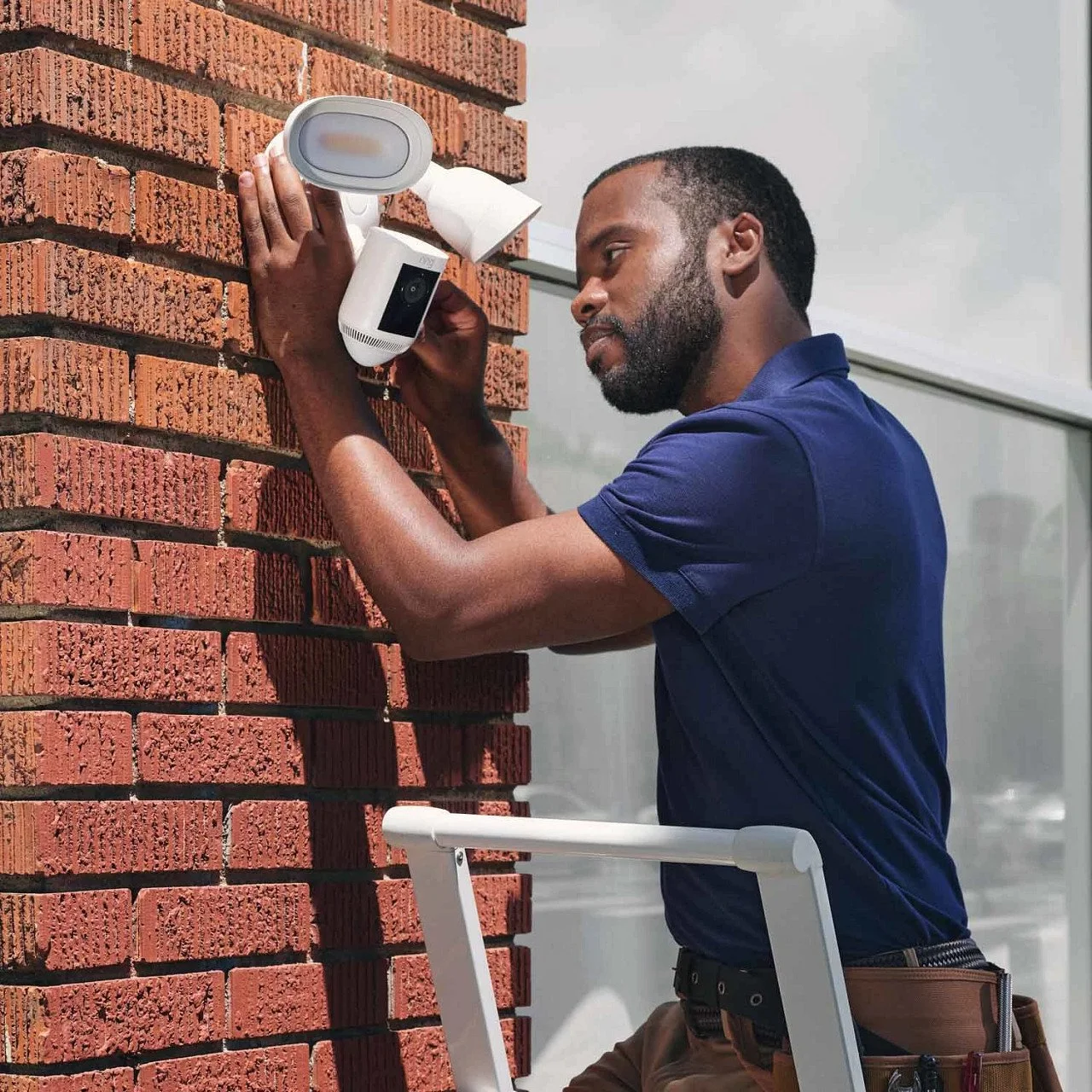 A technician installing a security camera on a brick wall outside a building.