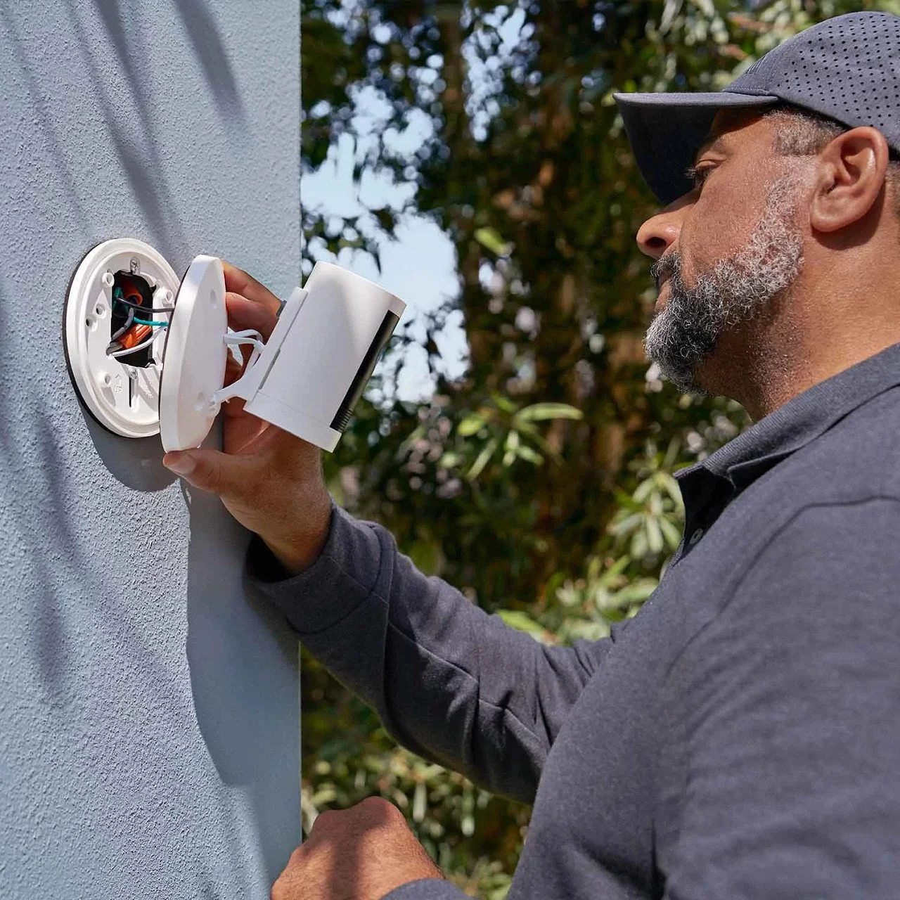 A man installing or repairing a security camera on a house wall outdoors.