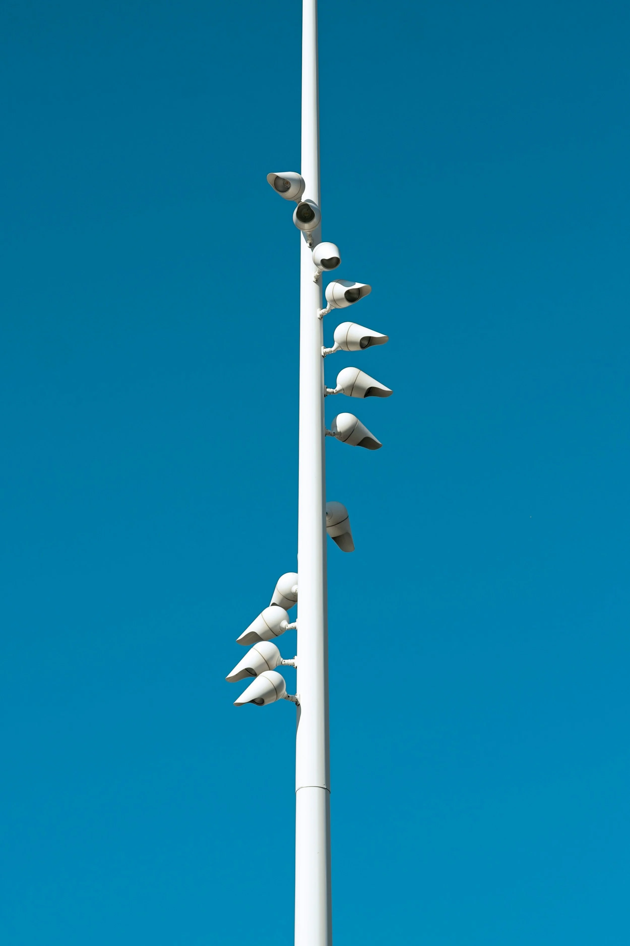 Tall white pole with multiple security cameras attached, set against a clear blue sky.