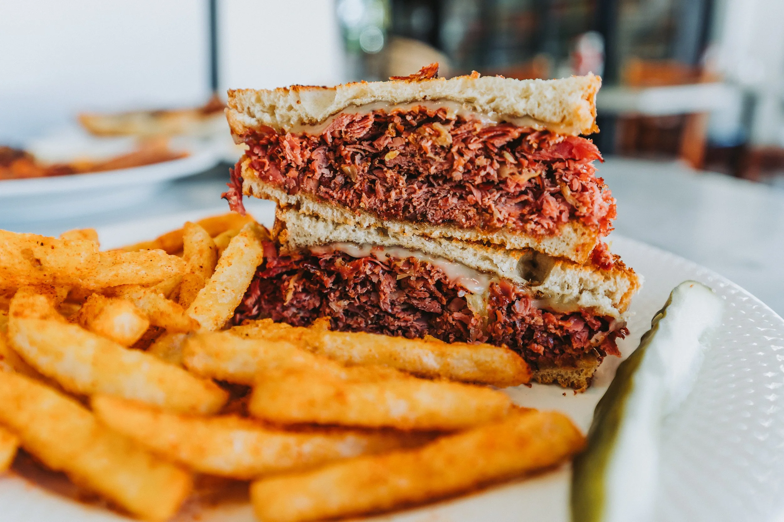 A sandwich with multiple layers of sliced deli meats and bread, served with French fries and a pickle spear on a white plate.