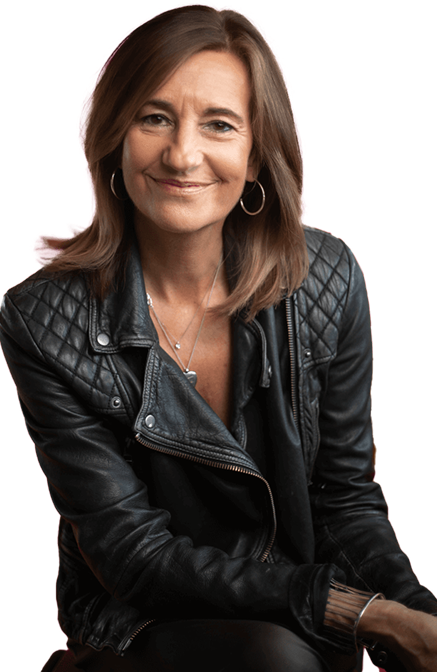 A woman with shoulder-length light brown hair, wearing a black leather jacket, silver hoop earrings, and a necklace, smiling at the camera with a neutral background.