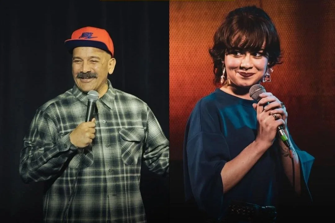 Two comedians, a man with a mustache wearing a plaid shirt and a red Nike cap, and a woman with short dark hair and earrings, holding microphones stand in front of dark backgrounds, smiling during a stand-up comedy performance.