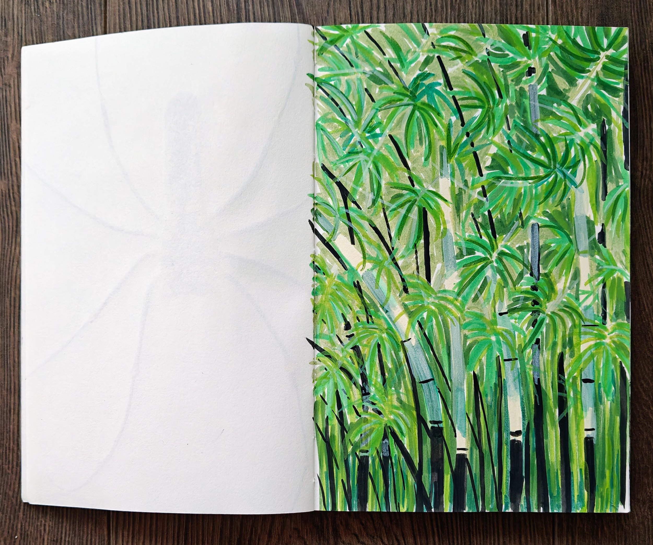Open sketchbook with left page blank and right page filled with a colorful, abstract painting of green leaves and black bamboo stalks, on a wooden surface.