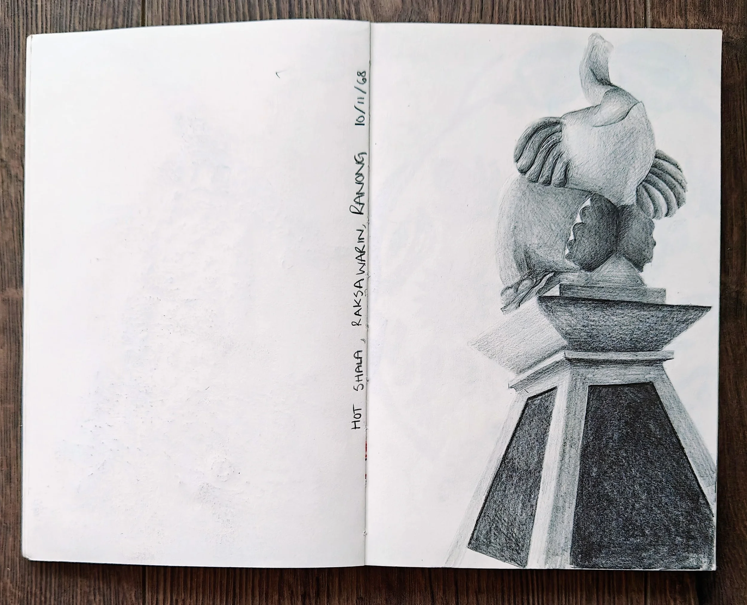 A grayscale pencil drawing of a cute statue of an elephant, placed on a pedestal with geometric shapes, on a wooden surface.