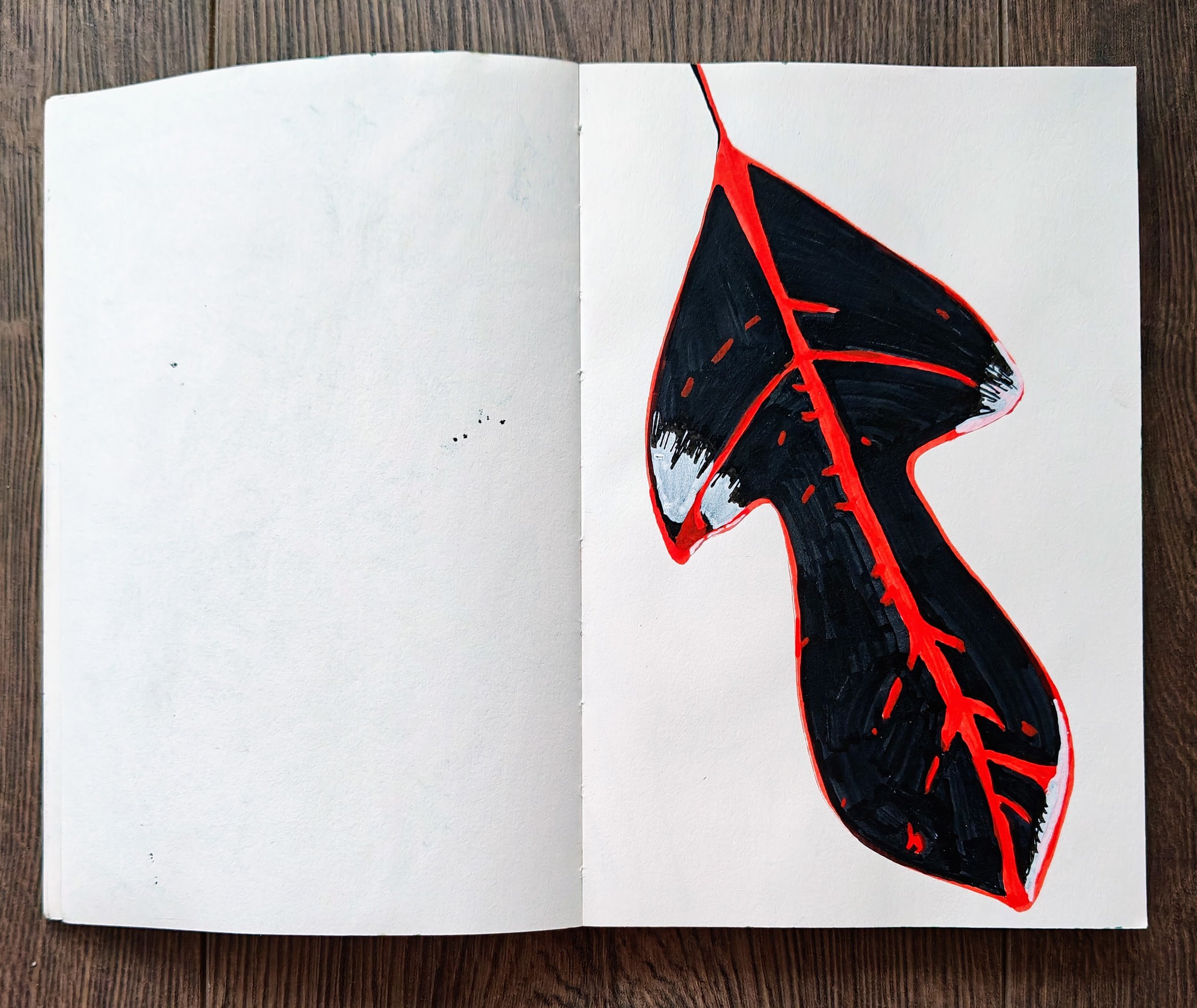 An open sketchbook with a drawing of a black leaf with red veins on white paper.