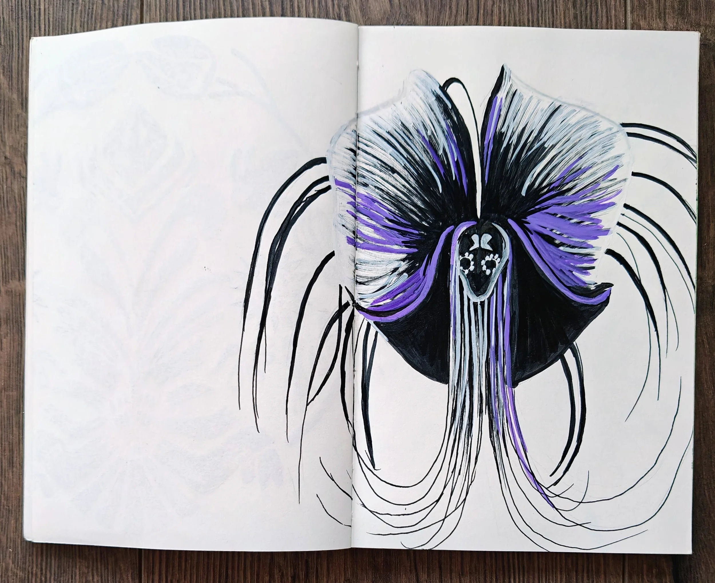 Open sketchbook with a stylized drawing of a black and purple orchid flower, with detailed petals and long, flowing lines, on a wooden surface.