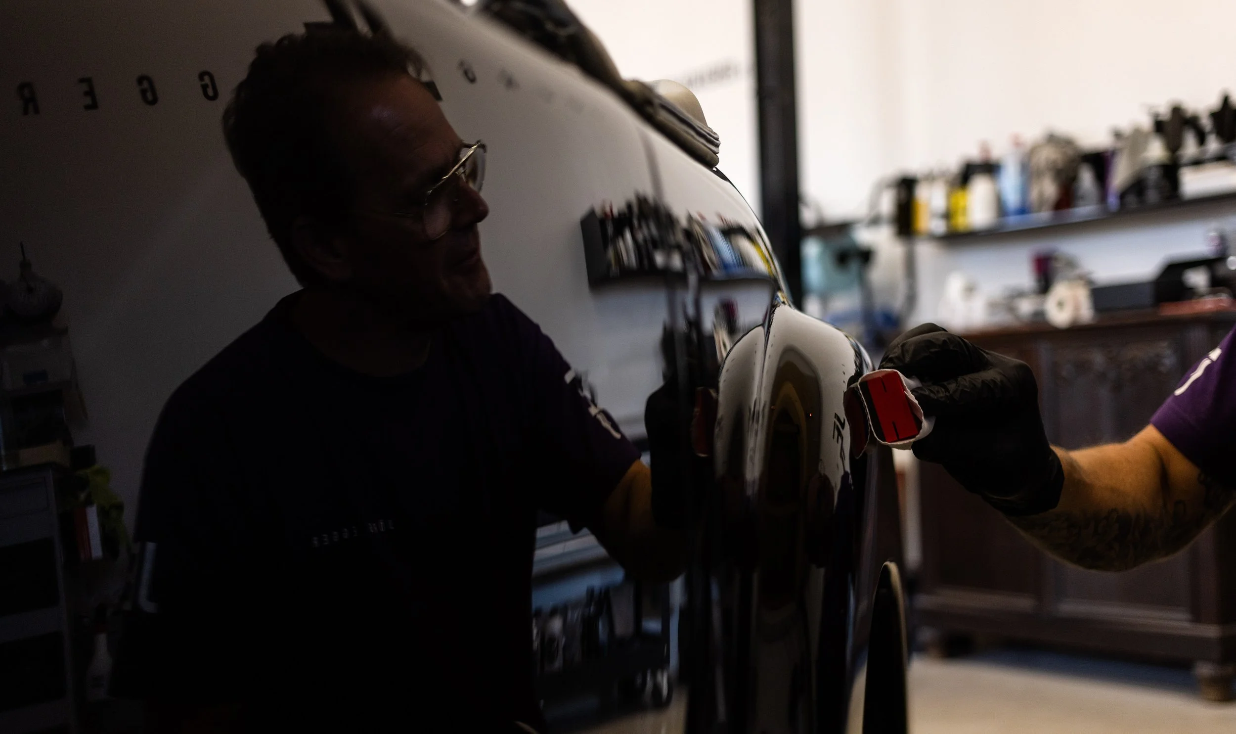 Lackierer bei der Arbeit am Triumph Roadster 2000 Oldtimer. Spiegelung im hochglänzenden schwarzen Lack während des Polierprozesses. Präzise Handarbeit bei der Restaurierung klassischer Fahrzeuge.