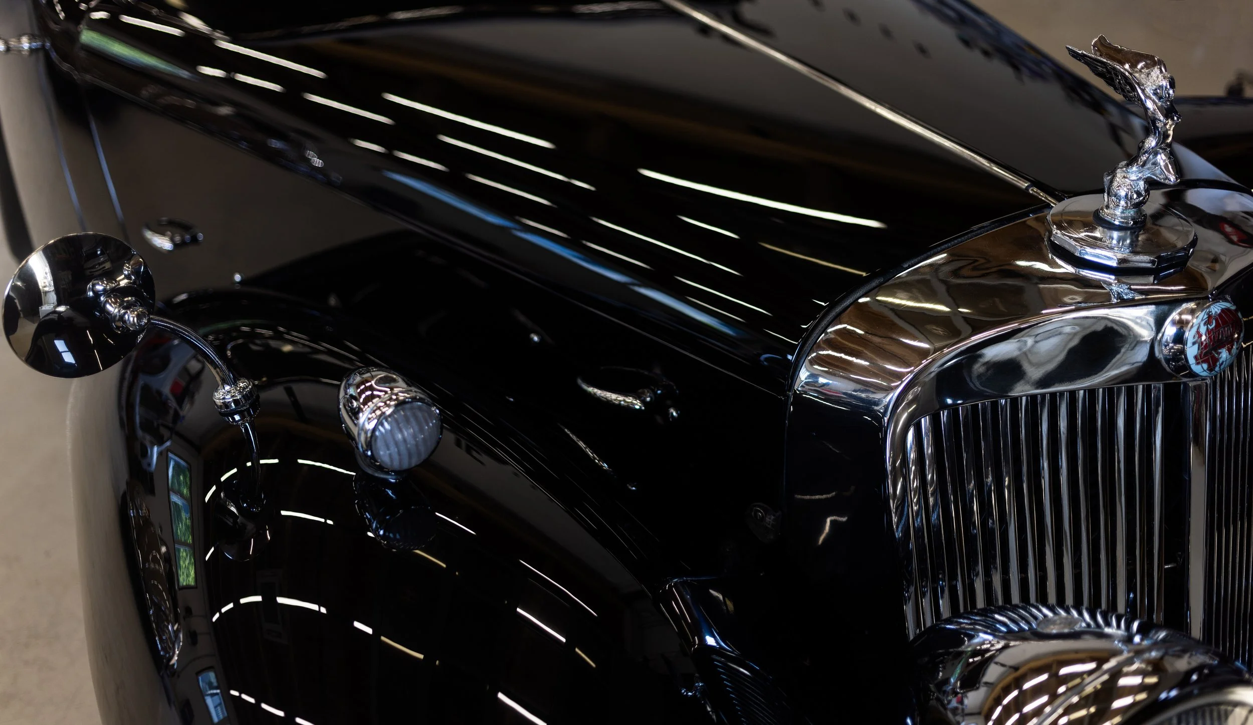 Triumph Roadster 2000 Oldtimer Detailaufnahme der Frontpartie. Hochglänzende schwarze Lackierung mit verchromtem Kühlergrill, Scheinwerfern und klassischer Kühlerfigur. Restauriertes Cabriolet als Beispiel präziser Lack- und Chromarbeit.