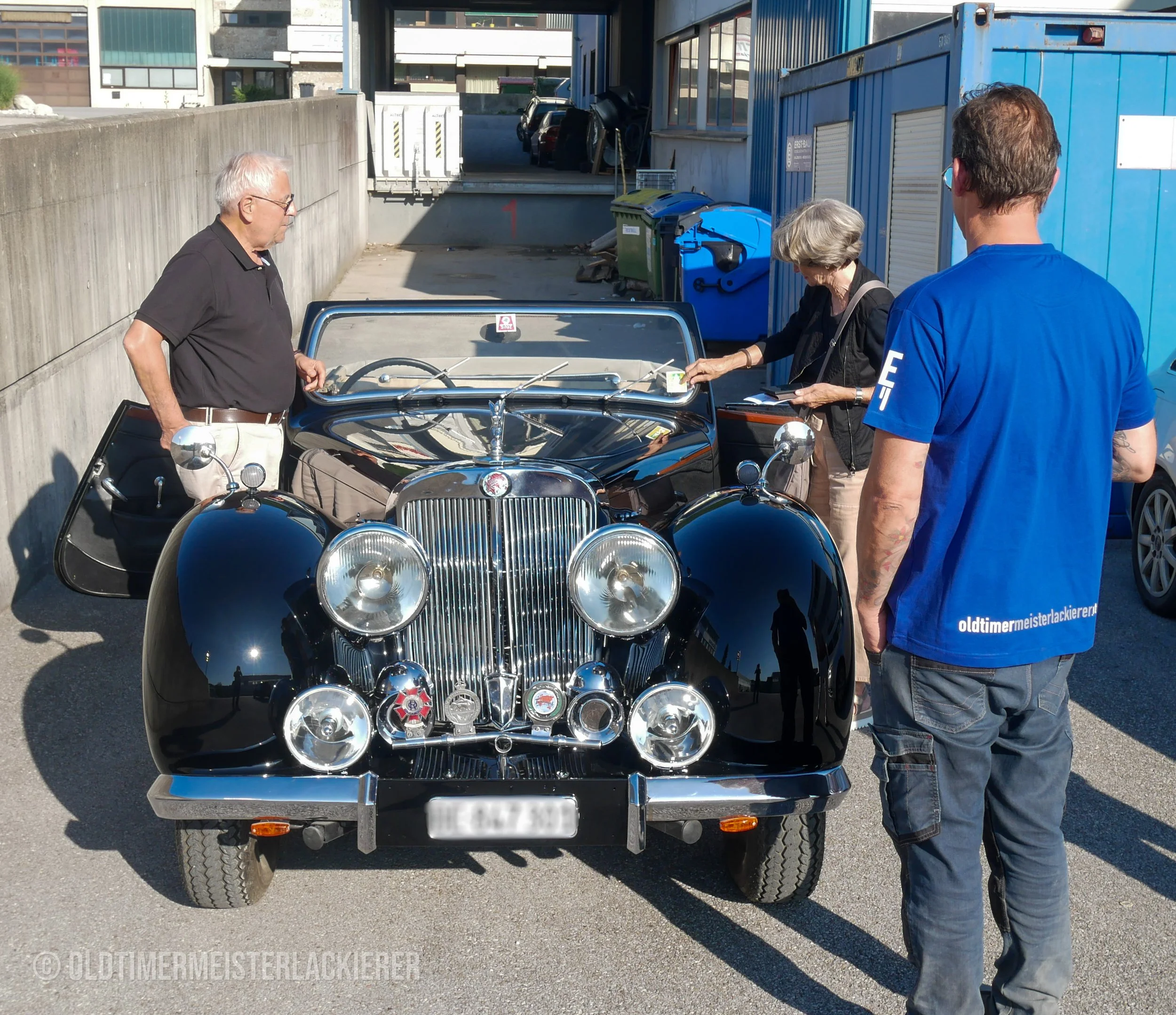 Übergabe eines Triumph Roadster 2000 nach Abschluss der hochwertigen Lackierungsarbeiten. Das Foto zeigt Kunden und Oldtimermeisterlackierer bei der persönlichen Fahrzeugübergabe vor der Werkstatt.