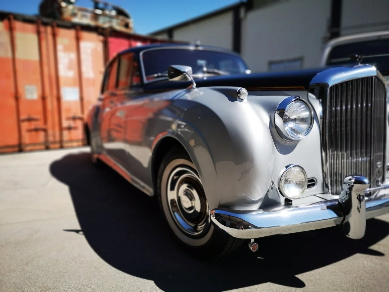 Bentley S1 James Young Oldtimer schräg von vorn fotografiert. Zweifarbige Lackierung in Silber und Schwarz mit glänzenden Chromdetails. Restaurierte Luxuslimousine der 1950er Jahre im Außenbereich bei Sonnenlicht.