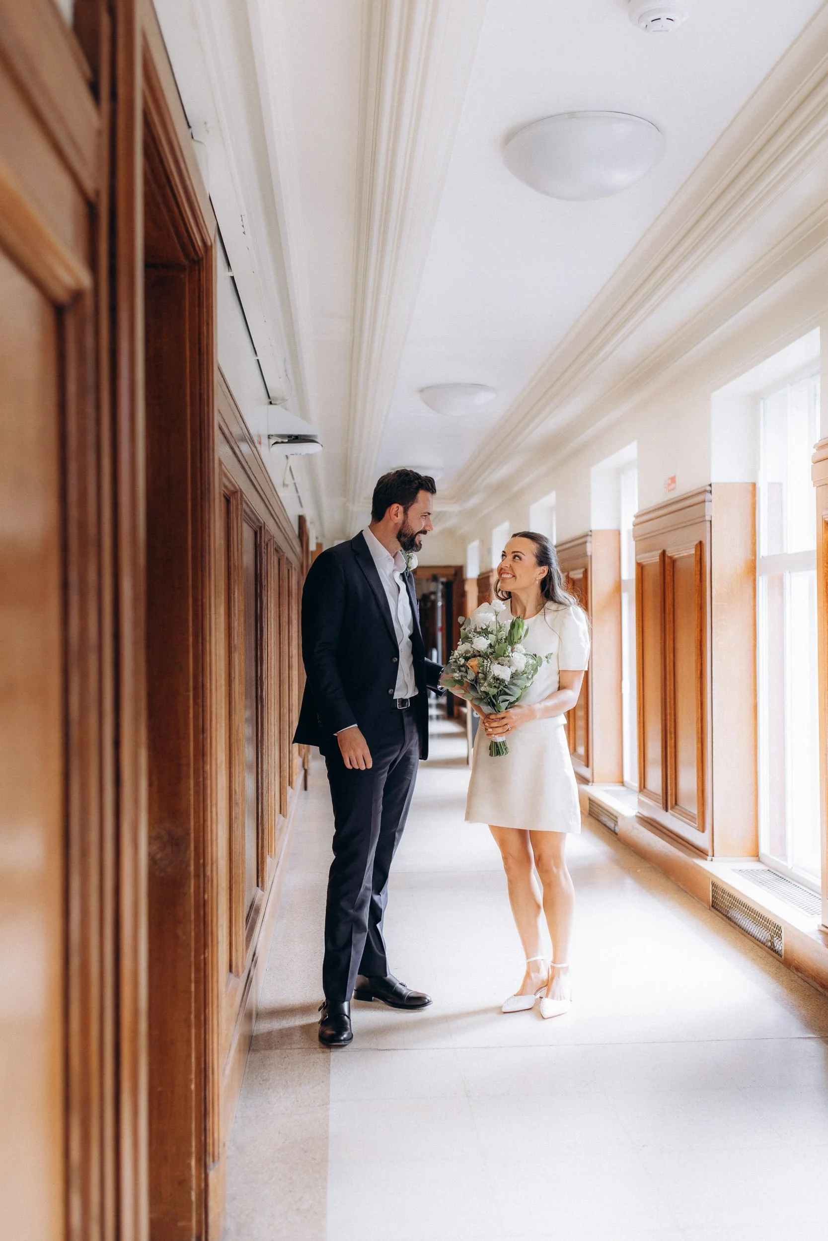 Bride and groom smiling at each other in the wood-panelled corridor at Wandsworth Town Hall