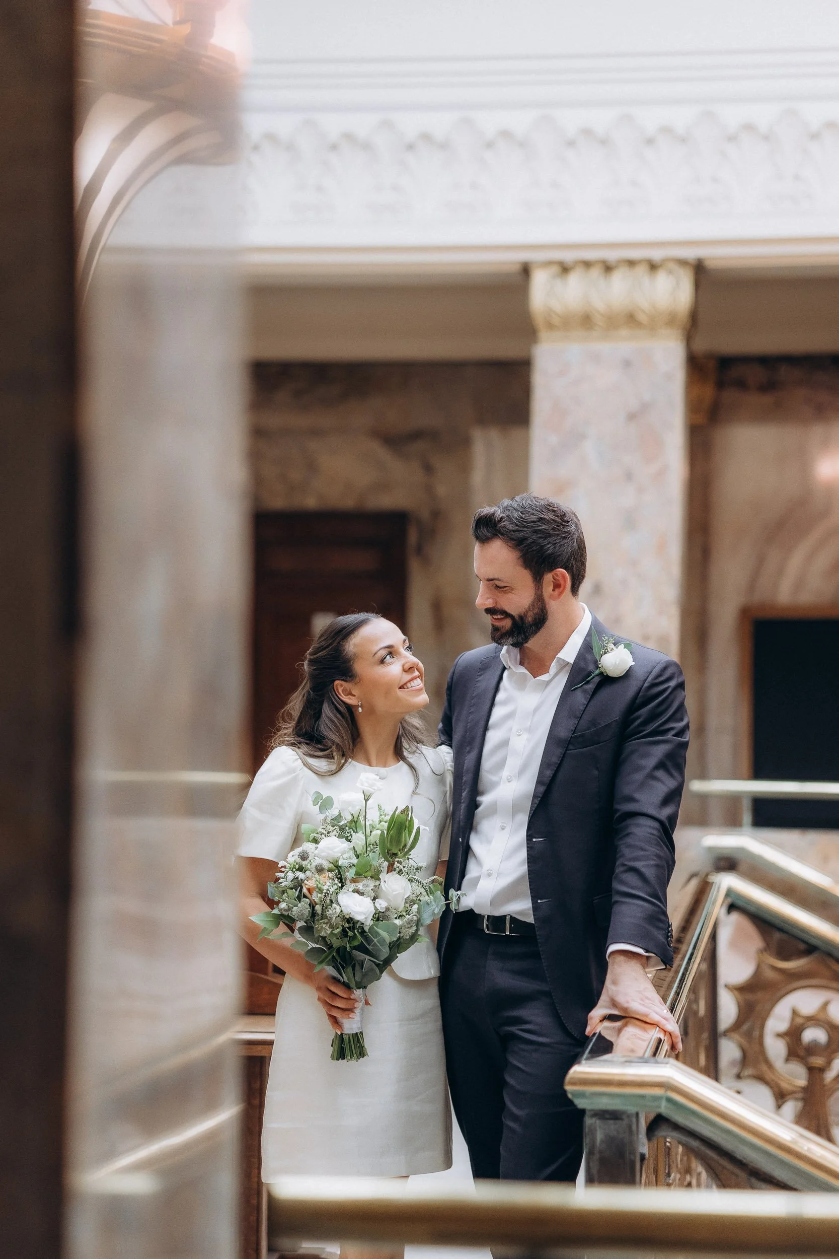  Couple smiling on the marble staircase landing between the columns of Wandsworth Town Hall 