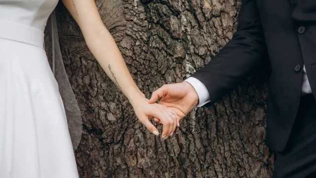 Close-up of the couple holding hands in front of a large tree trunk