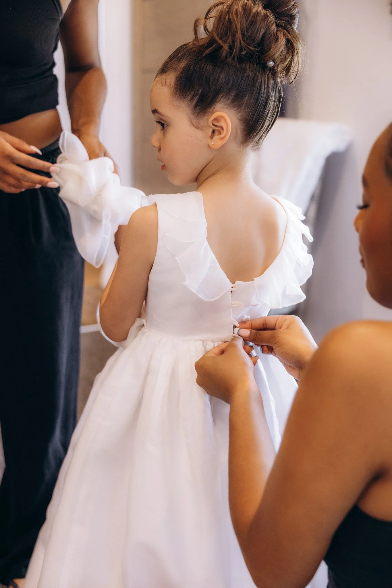 Bridesmaid fastening the back of a flower girl's white dress
