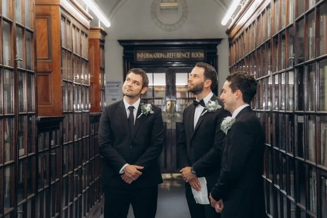 the groom and groomsmen in dark suits standing in a wood-panelled Fulham library room