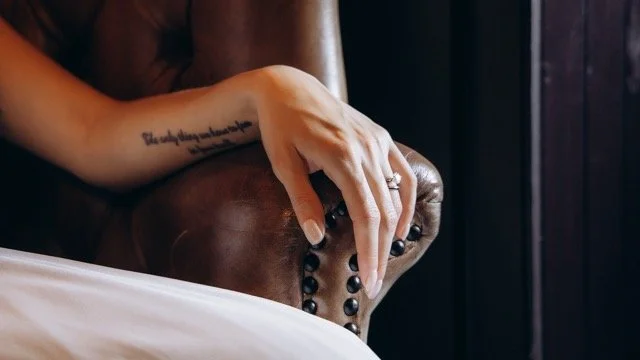 Close-up of the groom's hands with a rosary and a tattooed wrist resting on a leather chair