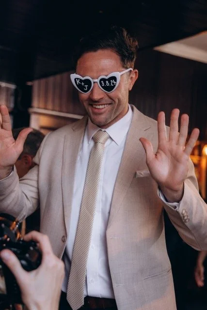 Male guest in a suit wearing heart-shaped sunglasses, waving at the camera