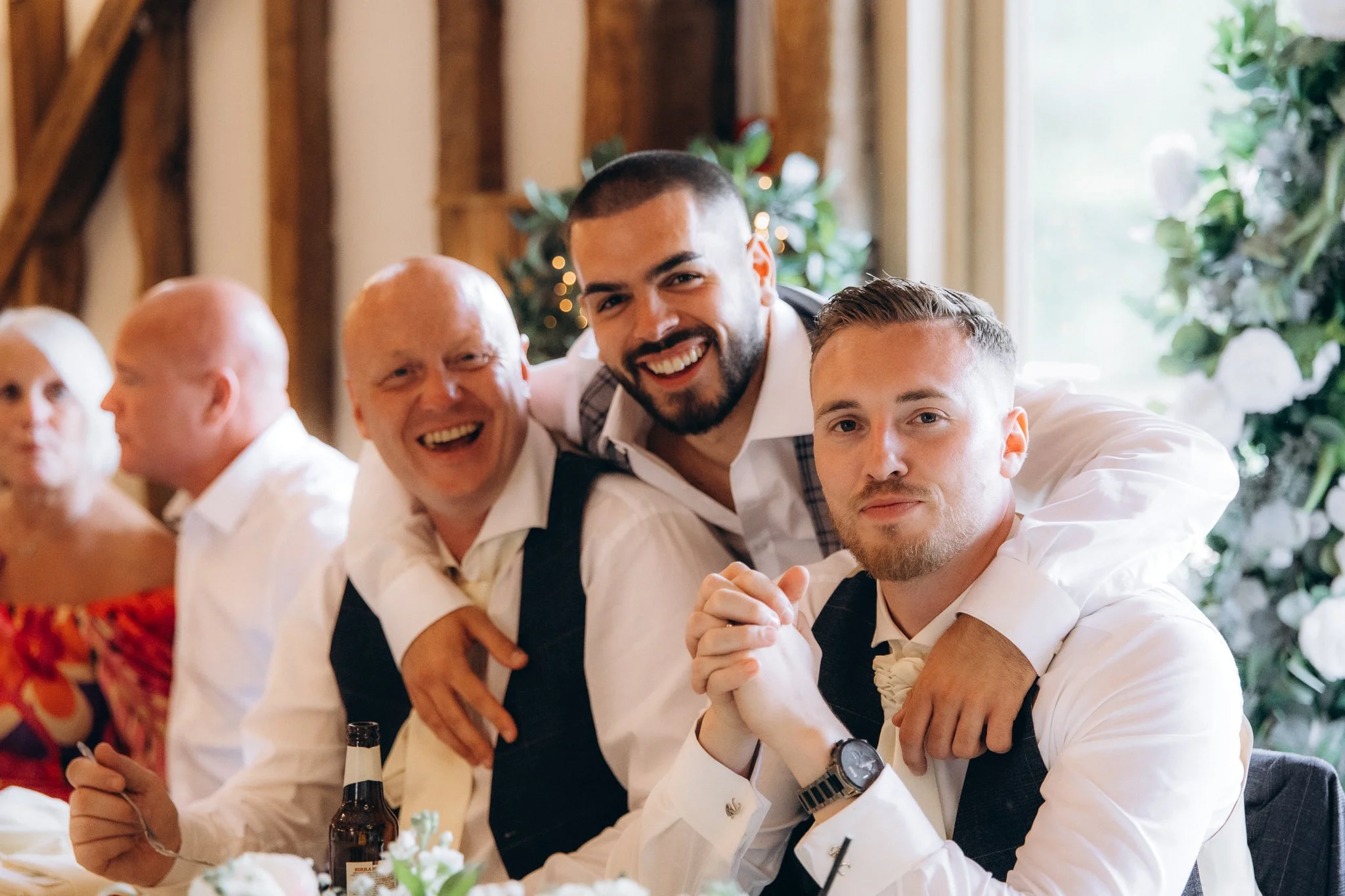 Two groomsmen laughing together with an older guest between them