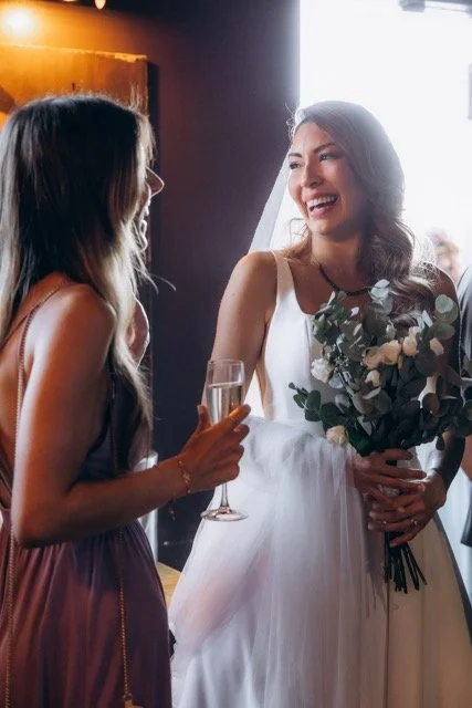  Bride laughing with champagne glass and white bouquet at her wedding reception — natural, unposed portrait by London documentary wedding photographer Lusy Klintsova 