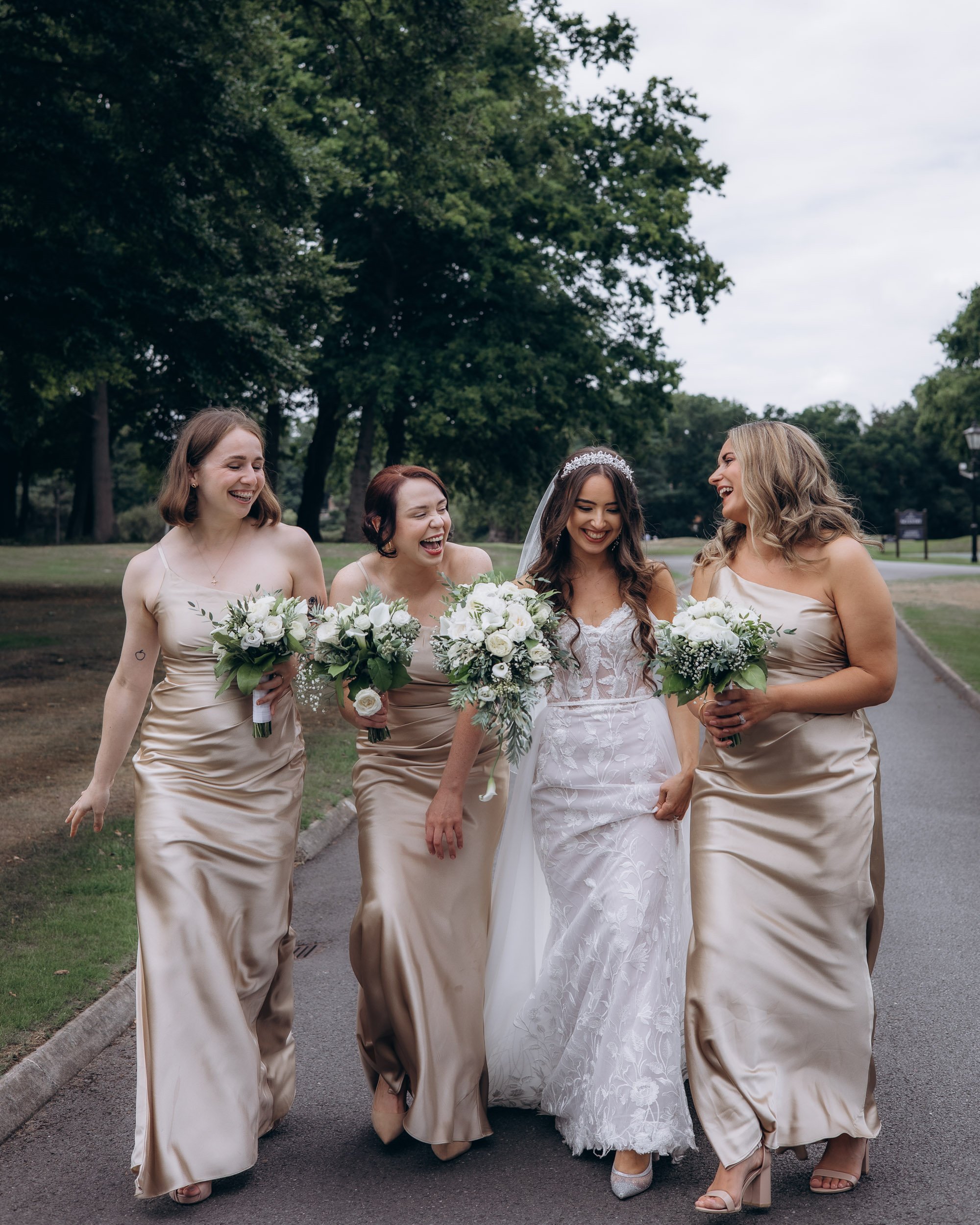 A relaxed and candid photo of bridesmaids in champagne silk dresses laughing together during a summer wedding win golf club.
