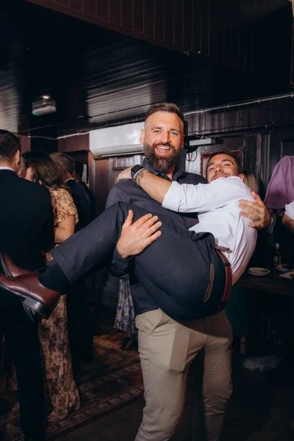 Two male guests playfully lifting each other in a bear hug on the dance floor