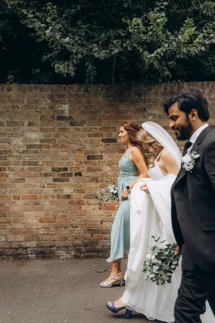 Bridesmaids and a guest laughing together against a brick wall