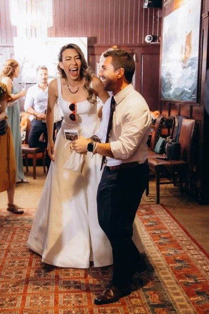 Male guest in a beige suit dancing and gesturing enthusiastically with bride
