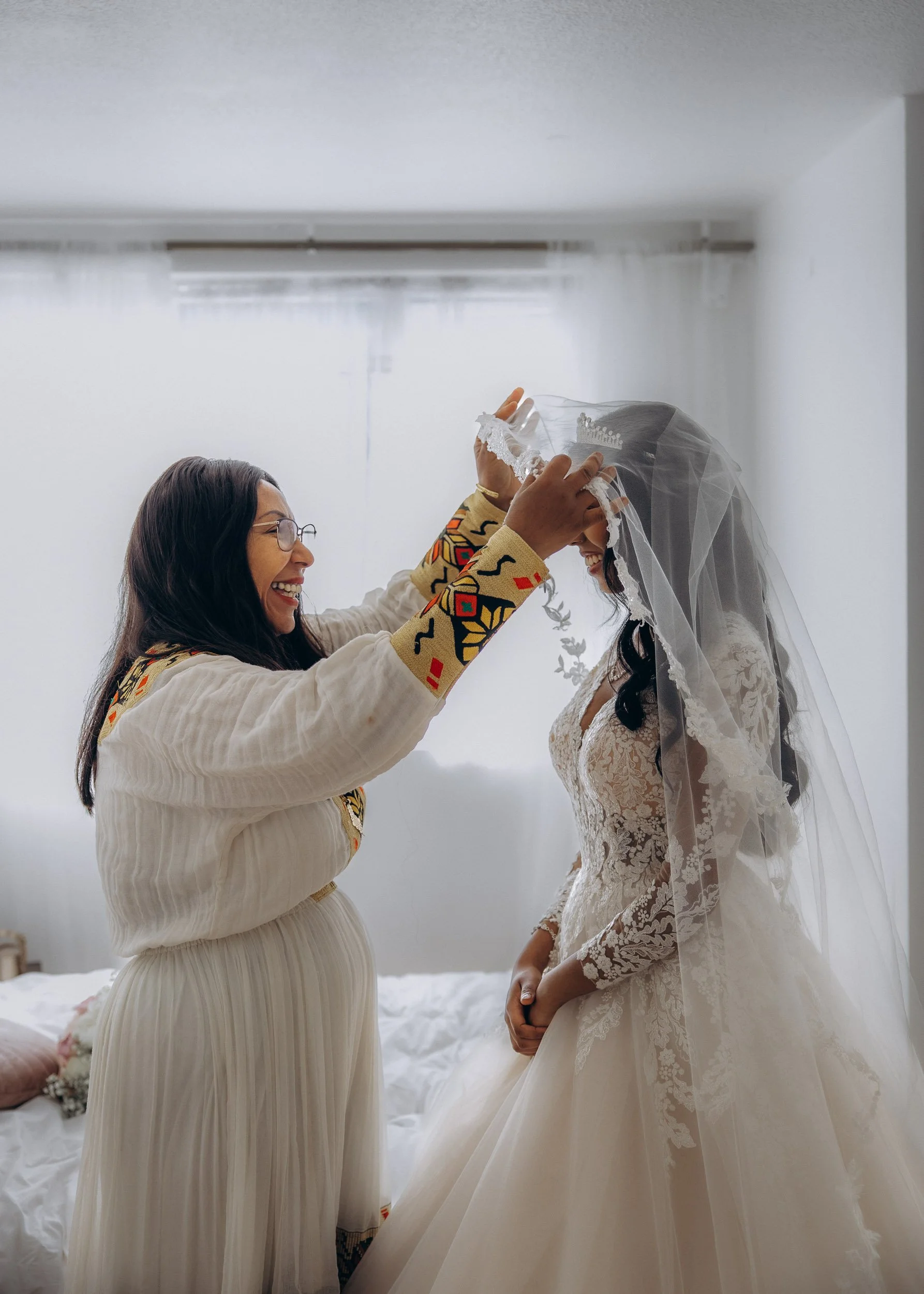 A detailed, documentary shot of mom carefully placing a traditional Ethiopian Orthodox ceremonial crown on the bride's head, showing a moment of cultural getting-ready tradition during a luxury wedding in London.