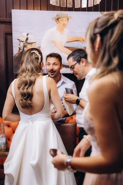 Bride on the dance floor, turned away from camera, with a male guest making a funny face